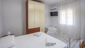 Une chambre à coucher avec un lit, une armoire, une télévision et une fenêtre avec des rideaux.