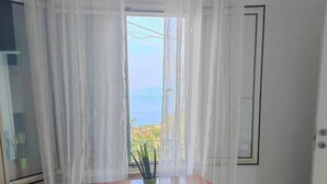 Une pièce avec un bureau et une chaise en bois, une fenêtre donnant sur la mer et des rideaux légers.