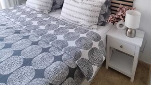 A bedroom with a bed, pillows, a nightstand, a lamp, and a woven wall decoration. - Casa Violette (Benissa)