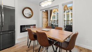 A modern kitchen with a wooden dining table, brown chairs, a stainless steel refrigerator, and a large mirror on the wall.