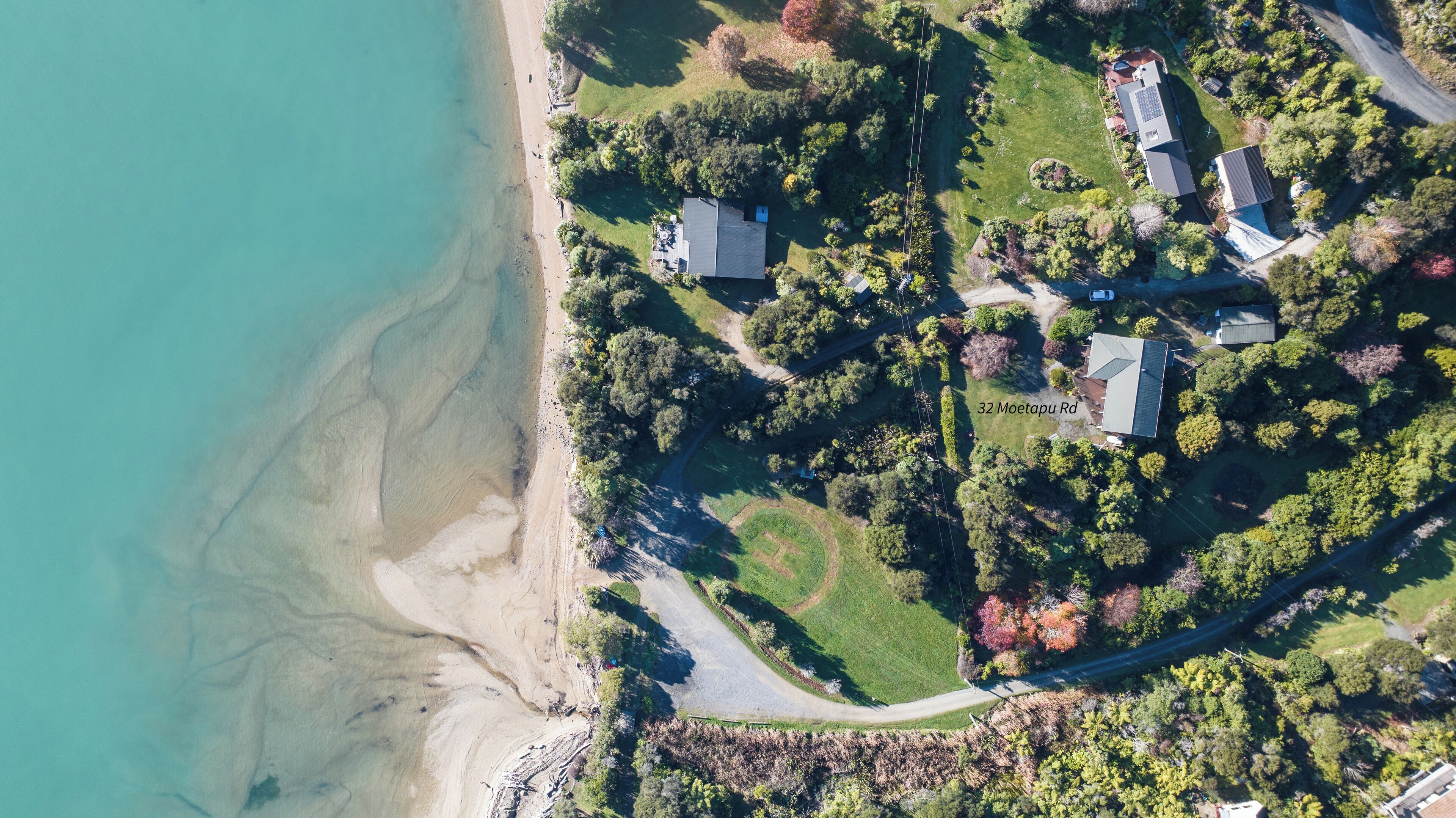 An aerial view of a coastal property with multiple houses, a beach, and a winding road.