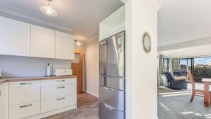 A modern kitchen with white cabinets, a stainless steel refrigerator, and a dining area with a table and chairs. - Moetapu Magic - Marlborough Sounds Holiday Home (Picton)