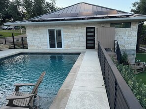 Ein modernes Haus mit Natursteinfassade, einem Swimmingpool und einer Holzterrasse mit Sitzgelegenheiten.