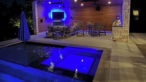 An outdoor pool area with a seating arrangement and a television screen mounted on a wall. - Hilltop Haven Retreat in Texas Hill Country.  Kid/Pet friendly.  Pool & Firepit (The Hills)