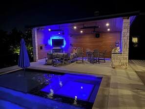 Un espace piscine extérieur aménagé avec des sièges et un écran de télévision fixé au mur.