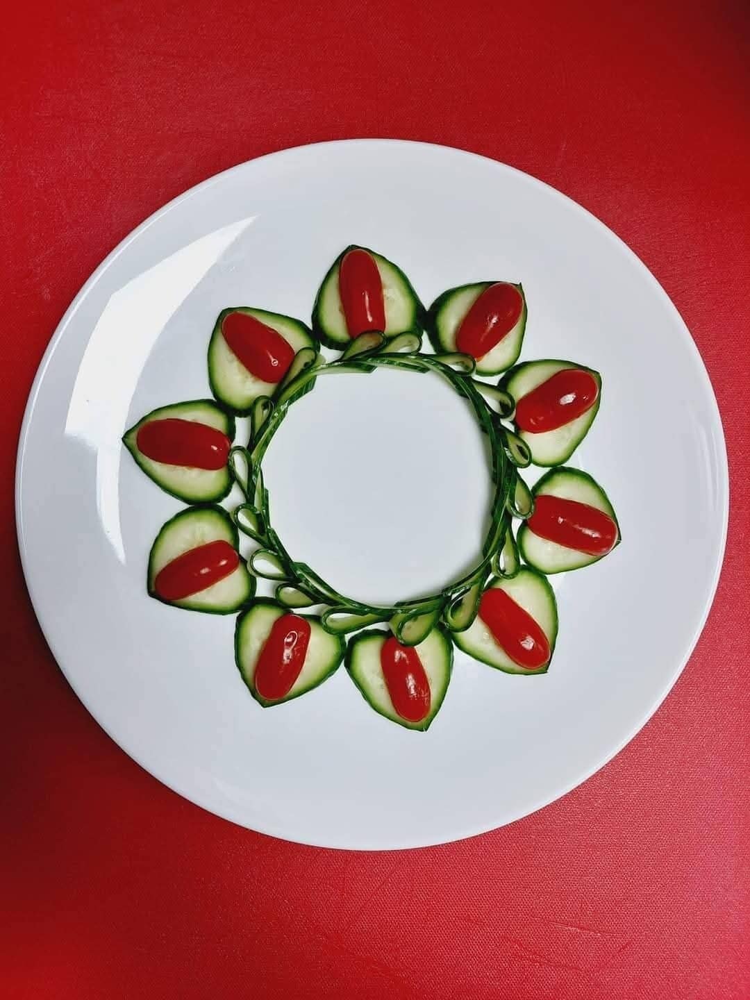 A white plate with a cucumber and tomato salad arranged in a circular pattern on a red surface.