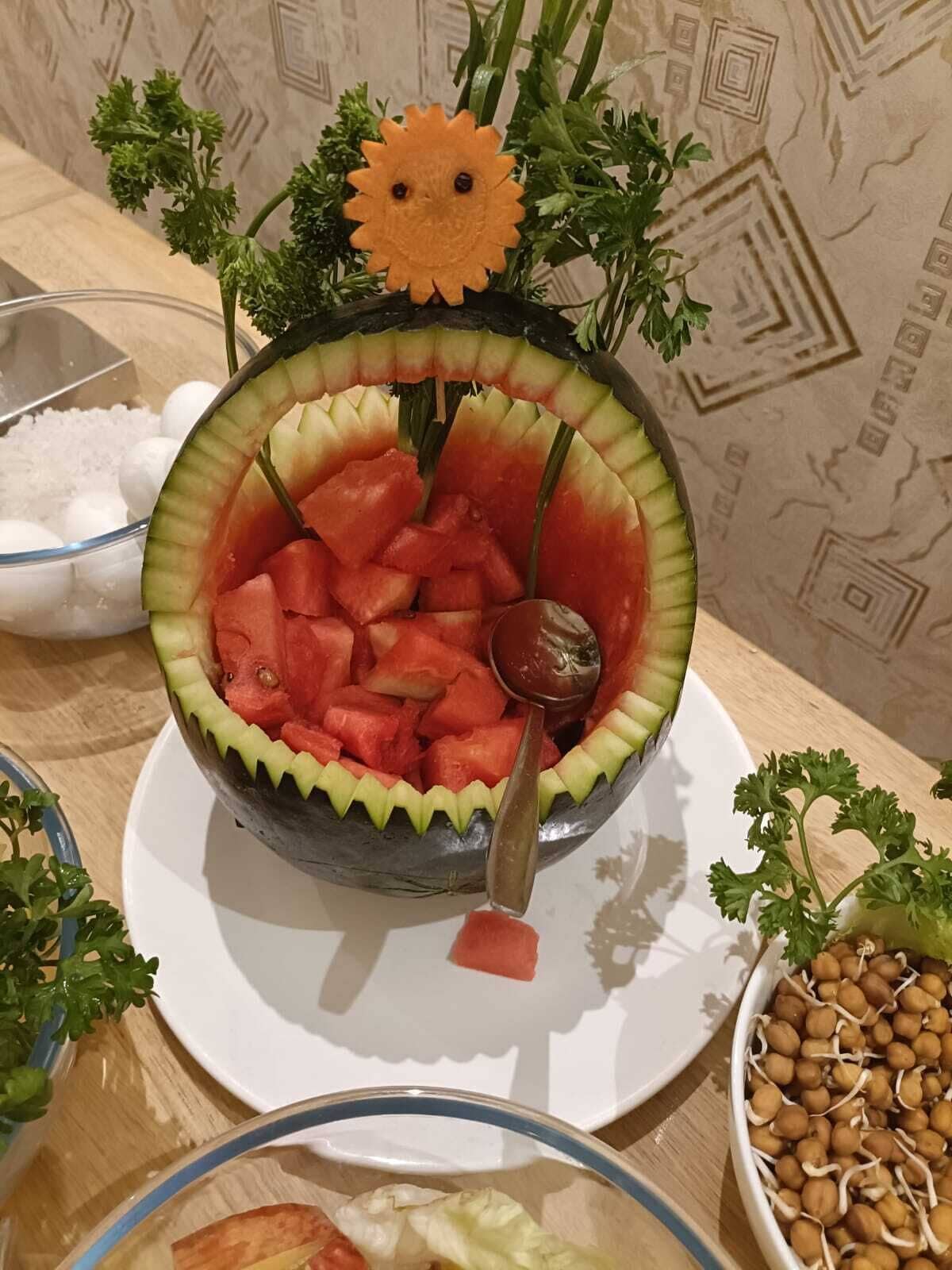 A bowl of watermelon salad with a decorative top, surrounded by parsley and chickpeas.