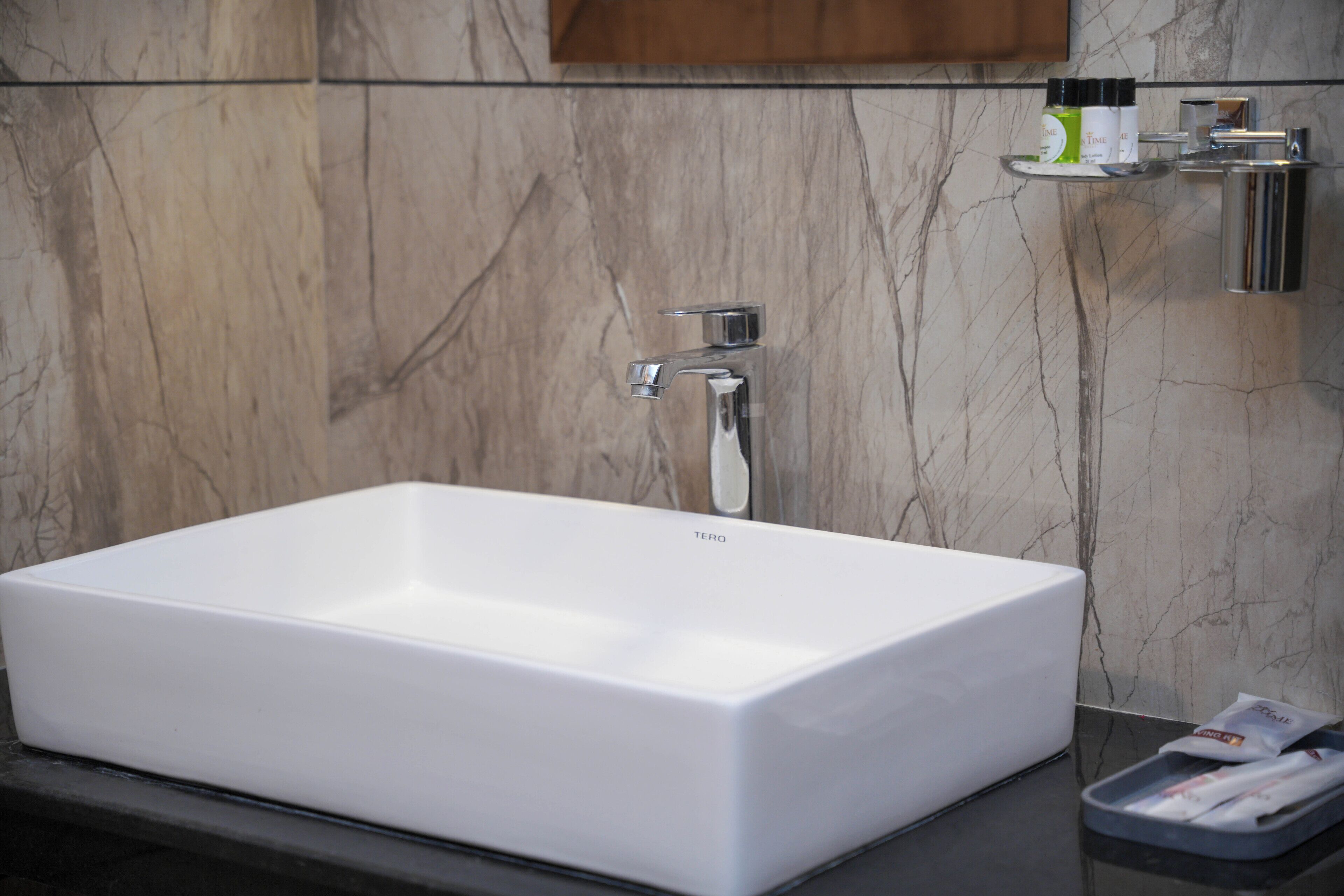 A white rectangular bathroom sink with a single faucet, set against a marble wall.