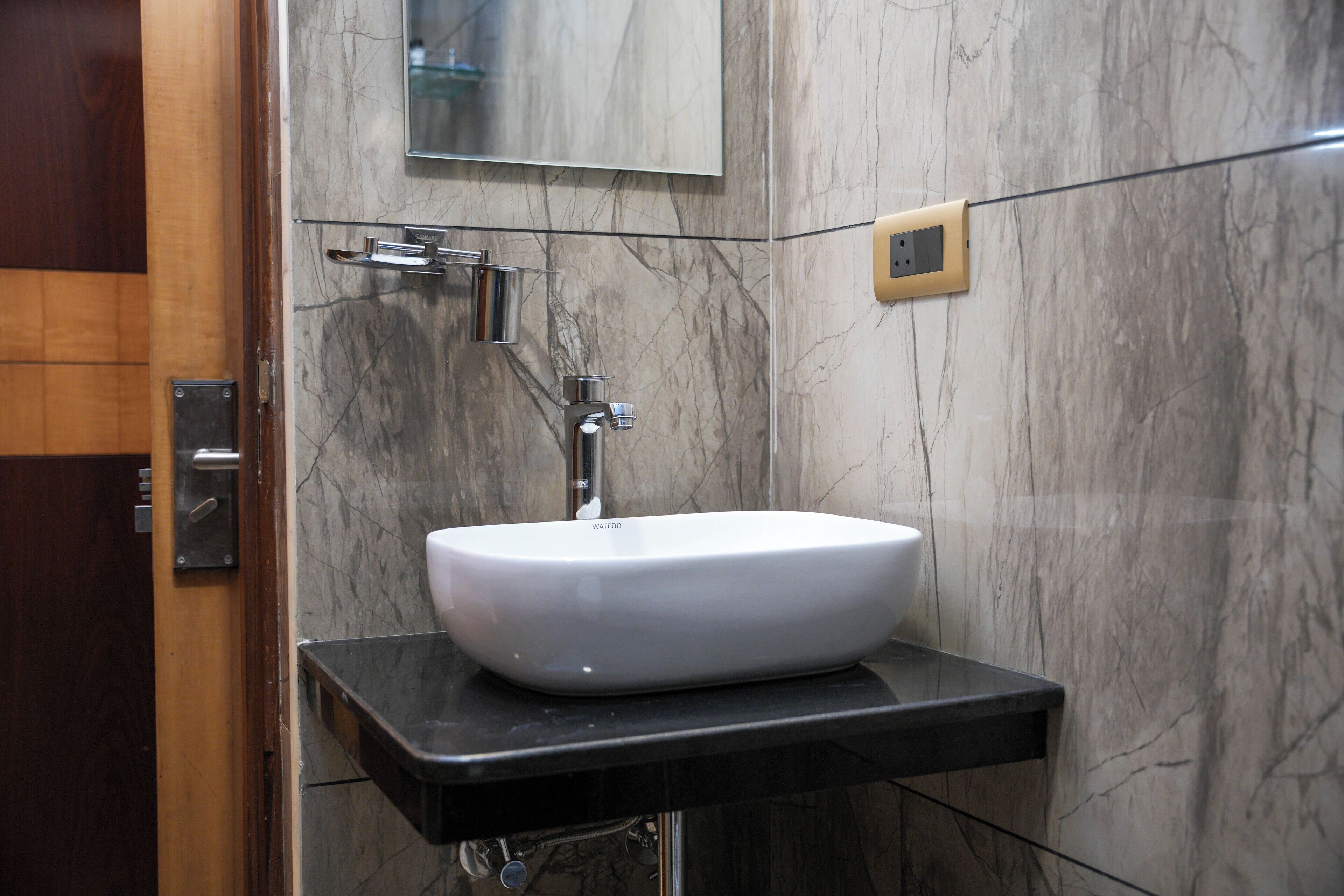 A bathroom with a white vessel sink, a mirror, and a marble wall.