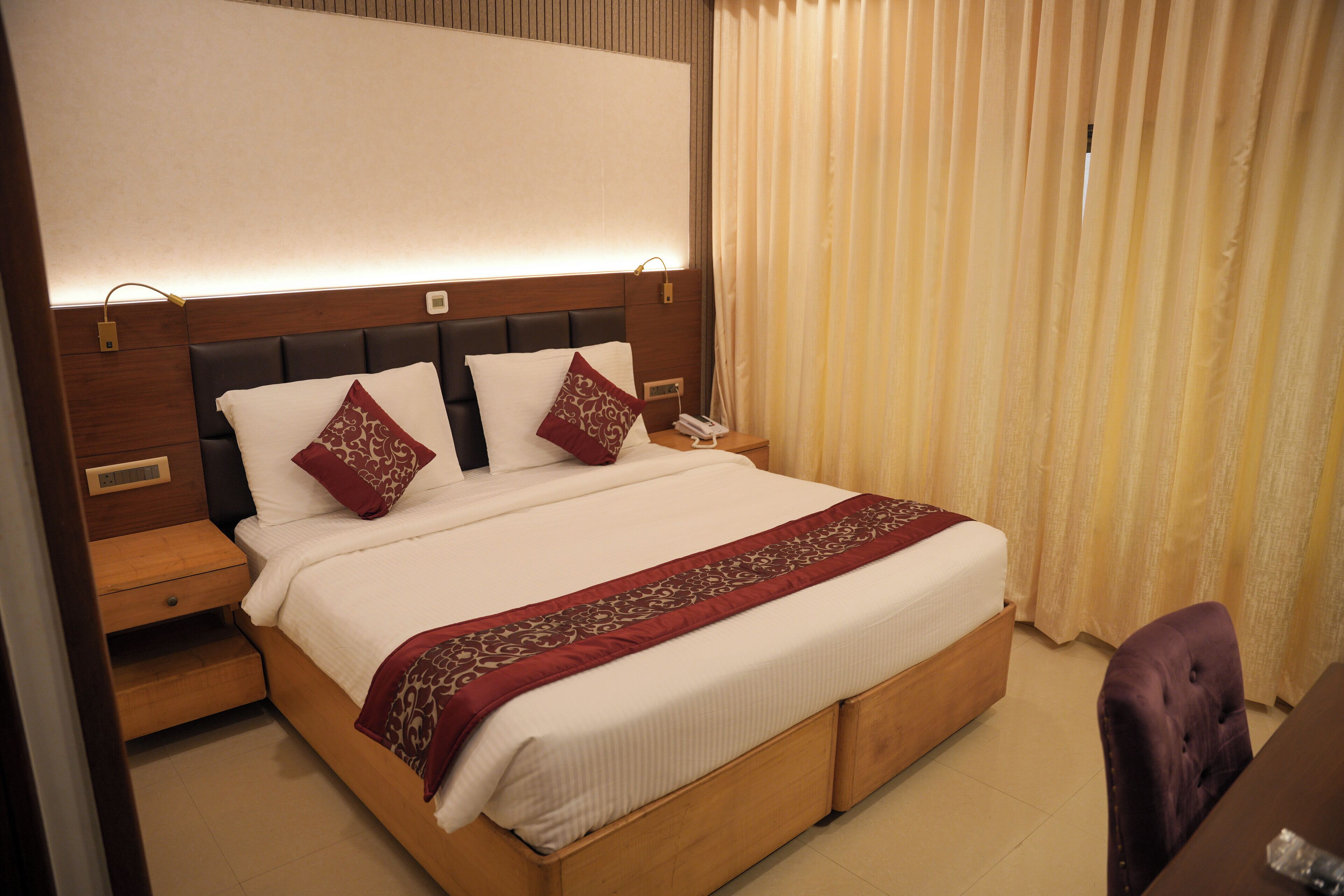 A neatly made bed with a wooden headboard, two bedside tables, and a purple chair.