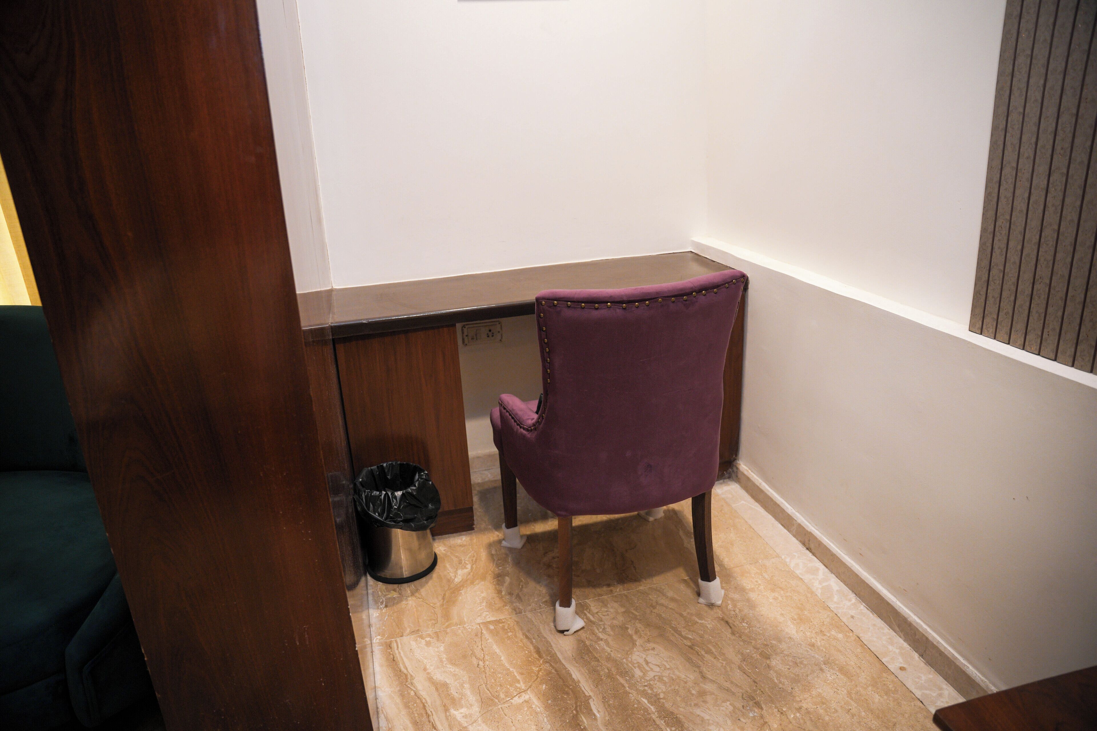 A corner of a room with a purple chair, a trash bin, and a wooden desk.