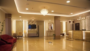 A modern lobby with a marble reception desk, a large chandelier, and red seating. - THE ON TIME HOTEL Bangalore (Bengaluru)