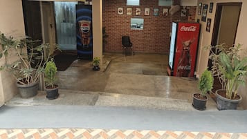 A lobby with a brick wall, a Pepsi advertisement, a Coca-Cola refrigerator, and potted plants.