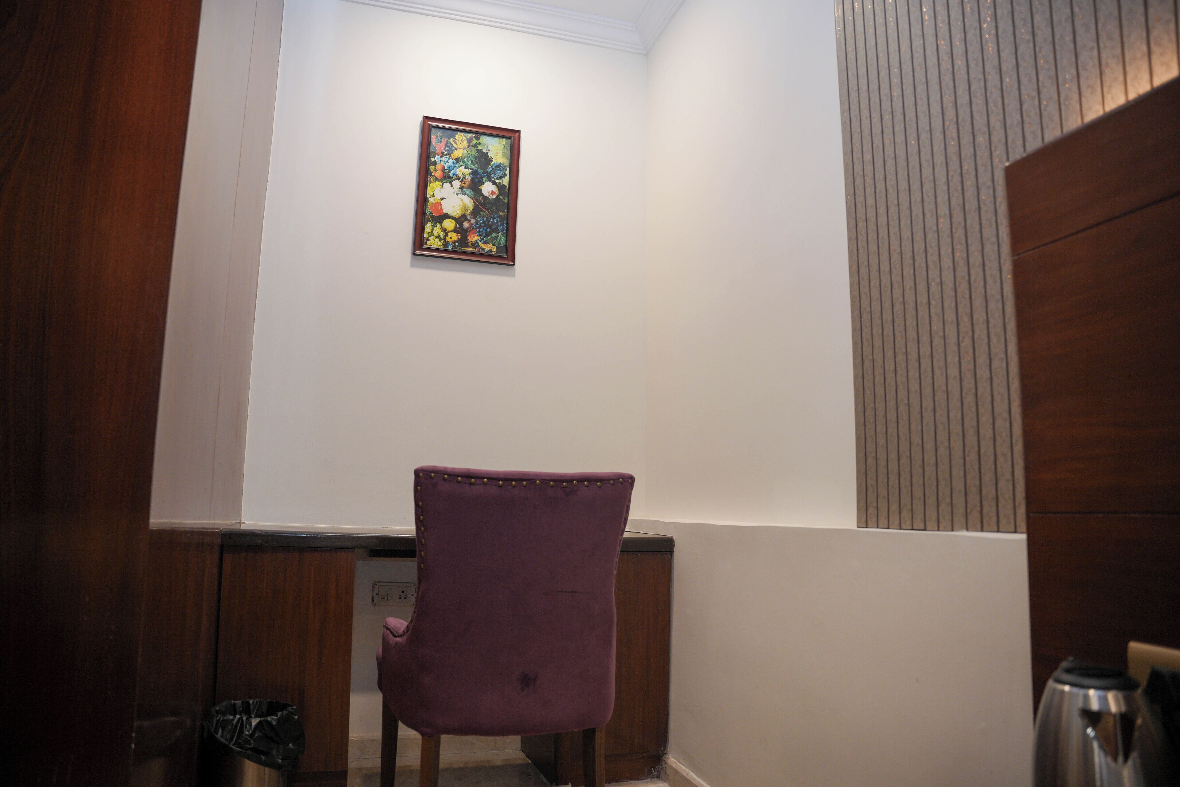 A corner of a room with a purple chair, a framed picture on the wall, and a wooden cabinet.