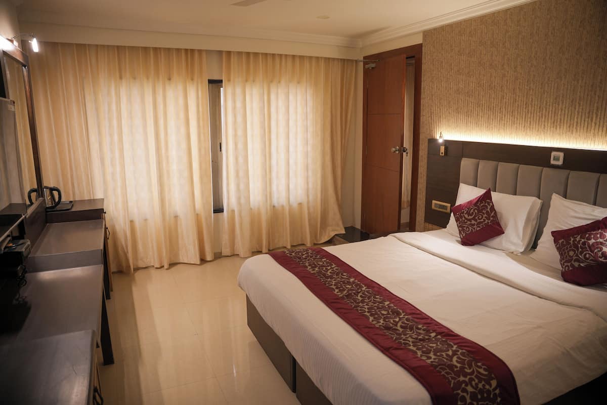 A hotel room with a large bed, a bedside table, a desk, and a window with curtains.