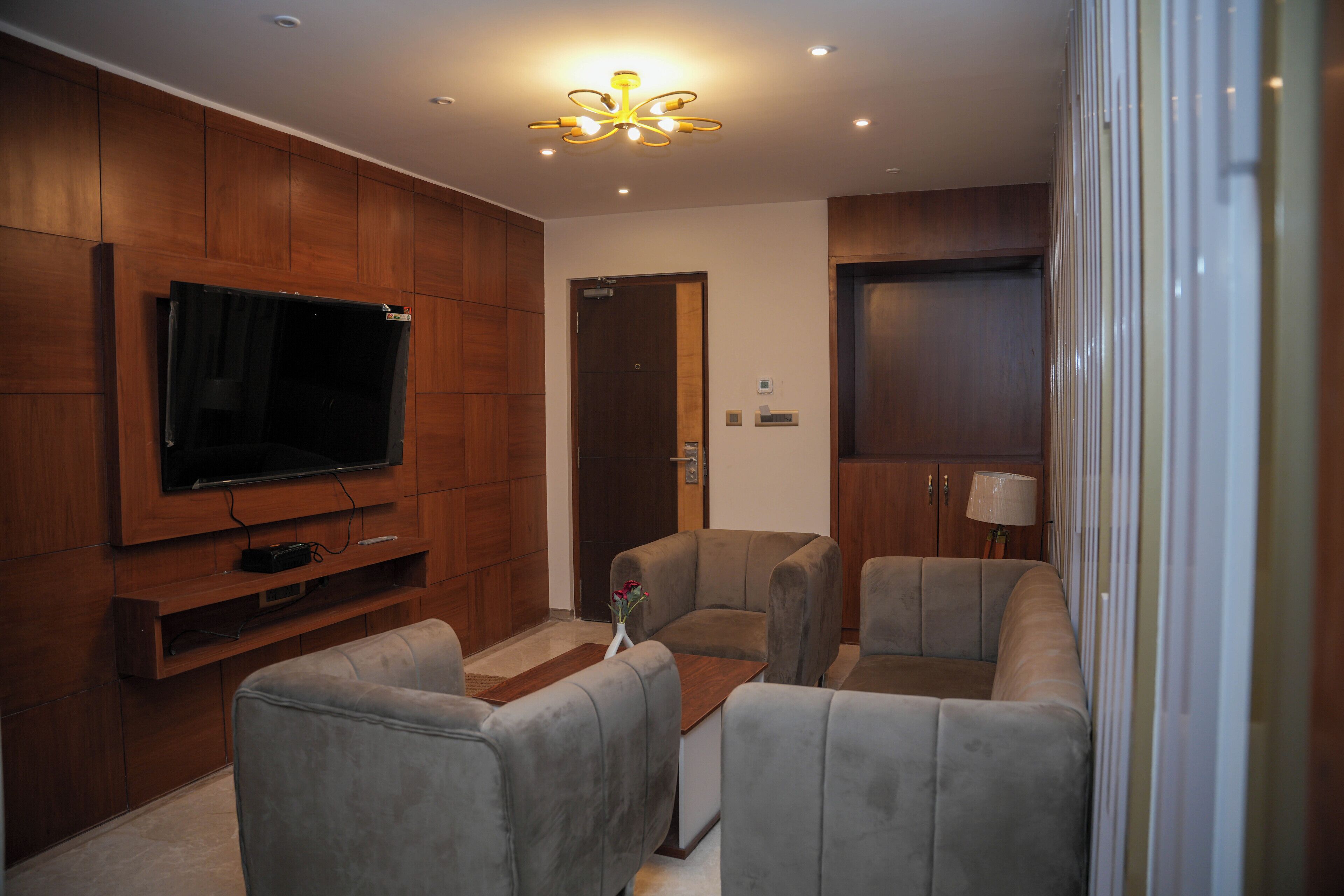 Ein modernes Wohnzimmer mit Flachbildfernseher, grauen Sofas, Holzvertäfelung und einer Deckenleuchte.