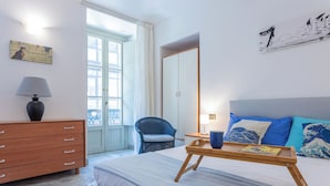 A hotel room with a bed, a wooden dresser, a chair, a window with curtains, and artwork on the walls. - Carlo Alberto House by Wonderful Italy (Turin)