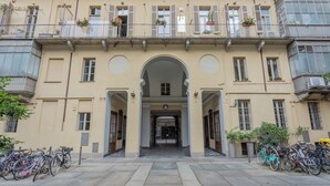 A building with a central archway entrance, multiple balconies with potted plants, and bicycles parked outside. - Carlo Alberto House by Wonderful Italy (Turin)