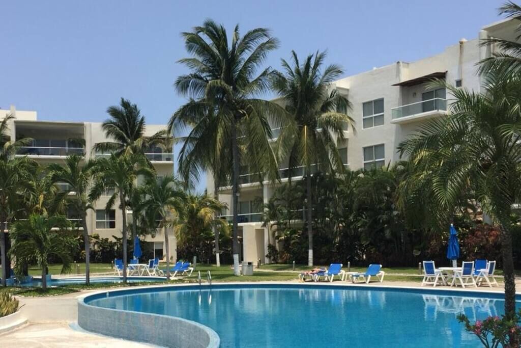 A pool area with lounge chairs and palm trees, surrounded by a building with balconies.