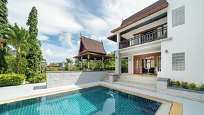 Ein modernes Haus mit Swimmingpool, Balkon und traditioneller Dachkonstruktion.