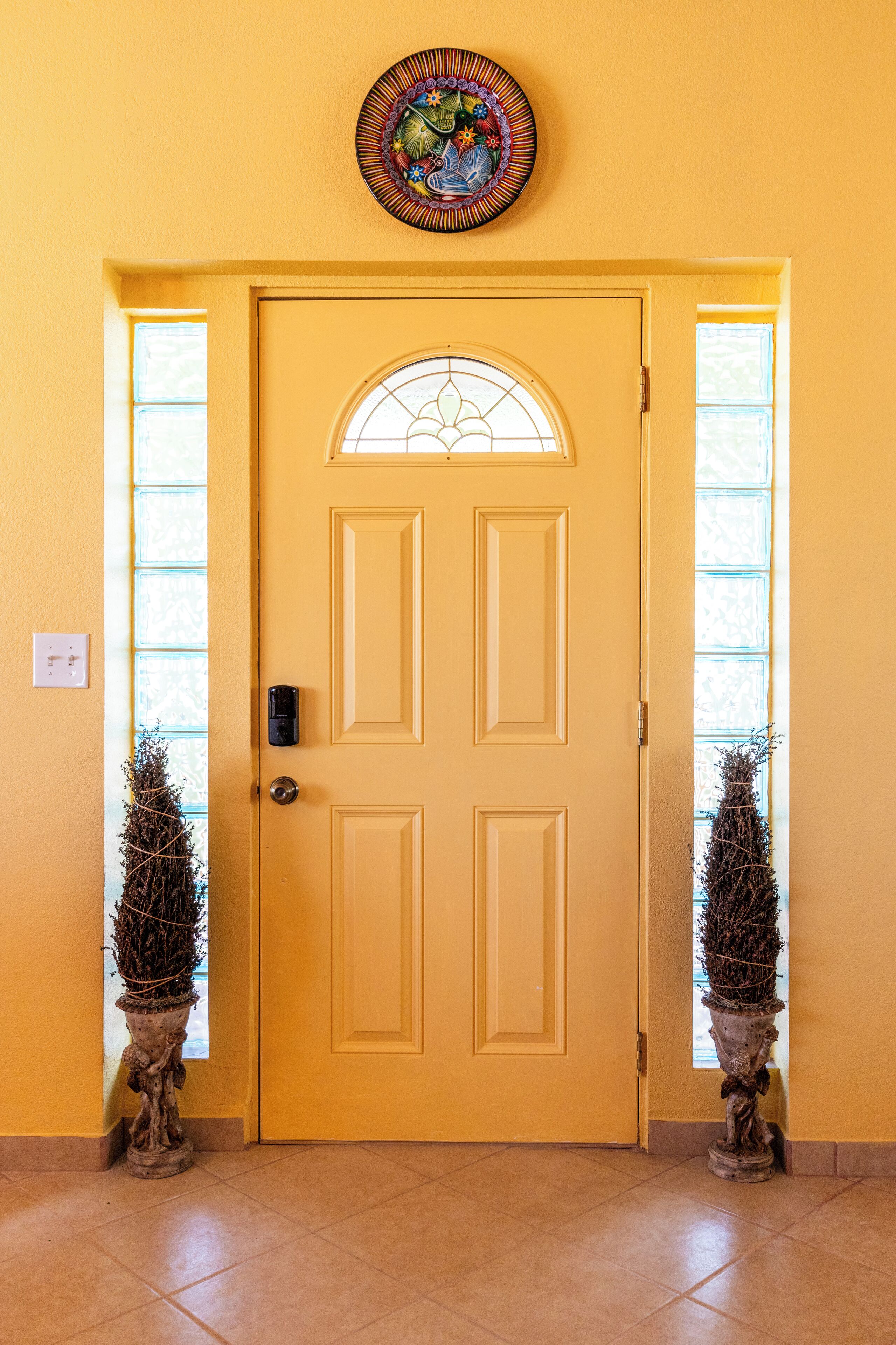 A yellow door with a decorative glass window above it, flanked by two potted plants.