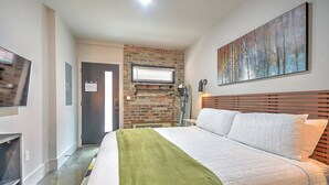 Ein Hotelzimmer mit Ziegelwand, einem großen Bett mit weißer Bettwäsche, einem Wand-Fernseher und einem Bild an der Wand.