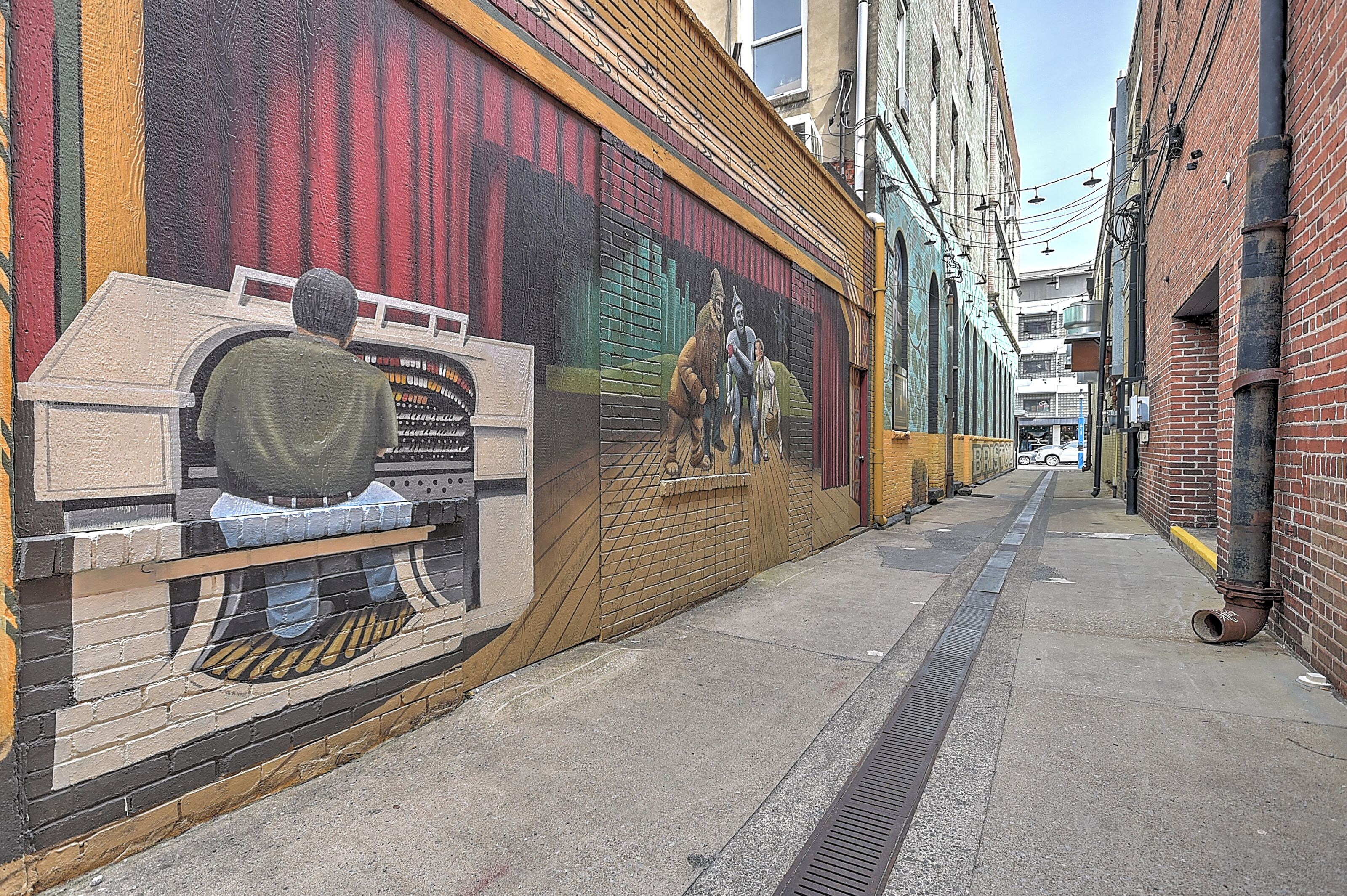 Un callejón estrecho con un mural en la pared izquierda que representa una escena histórica.