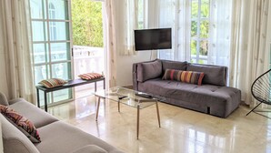 Uma sala de estar com um sofá cinzento, uma mesa de centro de vidro e uma TV na parede.