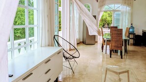 Quarto espaçoso com grandes janelas, ventilador de teto e área de jantar com cadeiras de vime.