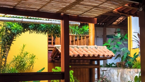 Ein überdachter Außenbereich mit einer Holz-Pergola, Kübelpflanzen und einer Steinmauer.