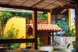 A covered outdoor area with a wooden pergola, potted plants, and a stone wall. - Pousada o Pharol (Itacaré)