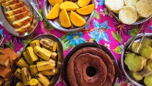 Verschiedene Lebensmittel, darunter Brot, Mangos, Bananen und ein Schokoladenkuchen, auf einer farbenfrohen Tischdecke.