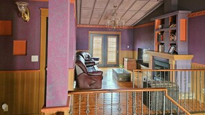 Uma sala de estar ampla com lareira, um sofá de couro e uma escada que leva a um andar superior.