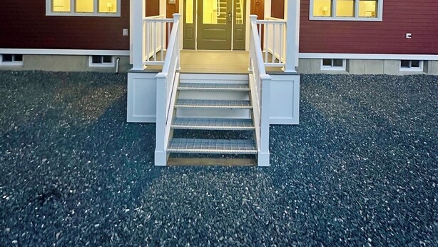 Un edificio de dos pisos con una entrada central, una escalera y un camino de grava.