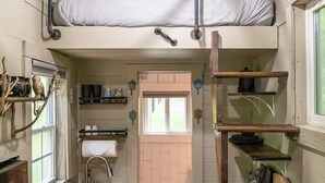 A compact kitchen with a wooden countertop, a sink, and a built-in oven. There is a bunk bed with a ladder and a hanging light fixture above it.