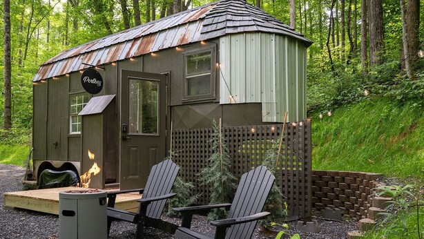 A rustic cabin with a metal roof, a wooden door, and a small porch with Adirondack chairs.