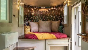 A cozy, compact room with a built-in bed, a small table, a chest of drawers, and a decorative wall.