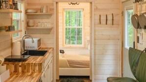 A compact cabin interior with a kitchenette, a bed, and a green sofa. - Serene, Romantic Getaway, Outdoor Shower, and Hiking! (Sylva)