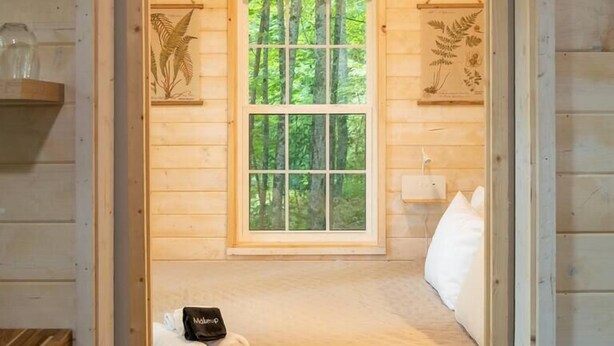A wooden cabin bedroom with a bed, pillows, a blanket, and a window with a forest view. - Serene, Romantic Getaway, Outdoor Shower, and Hiking! (Sylva)