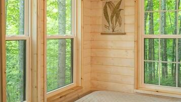 Une pièce de style cabane en bois, dotée de grandes fenêtres, d’un lit, d’une décoration murale représentant une tête de cerf et d’une œuvre d’art représentant une fougère.