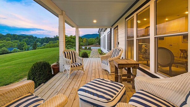 Eine überdachte Veranda mit Korbmöbeln, einem Holztisch und Blick auf eine grüne Landschaft.