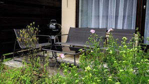 Un patio con un sofá exterior negro y una mesa, rodeado de follaje y flores.