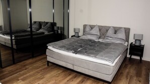 Un dormitorio moderno con una cama grande, una mesita de noche, un espejo y suelo de madera.