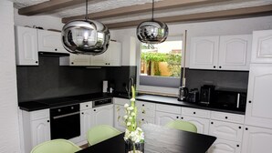 Una cocina moderna con armarios blancos, encimeras negras y una mesa de comedor con sillas verdes.