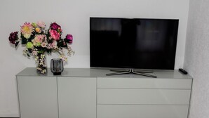 Un mueble moderno para entretenimiento con un televisor de pantalla plana, un jarrón de flores y un control remoto.