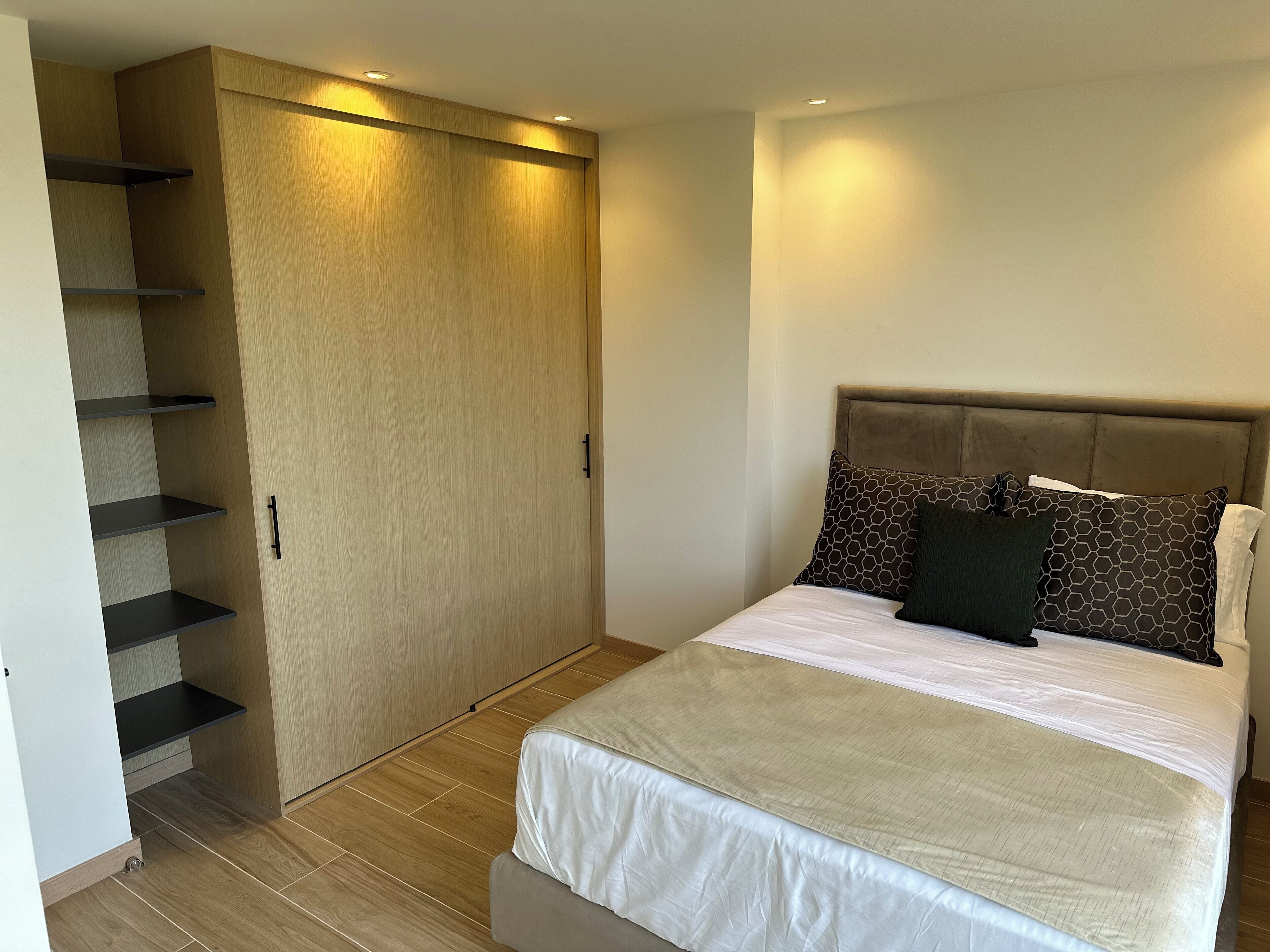 A bedroom with a bed, a headboard, a wardrobe with shelves, and a built-in bench.