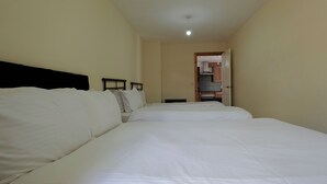A hotel room with a large bed, a bedside table, and a view of the kitchen through an open door. - The Serenity Apartment (Manchester)