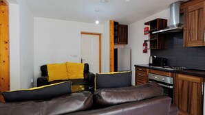 A compact living space with a sofa, a small kitchen area, and a door leading to another room. - The Serenity Apartment (Manchester)