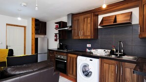 A compact kitchen with wooden cabinets, a built-in oven, a washing machine, and a sink. - The Serenity Apartment (Manchester)