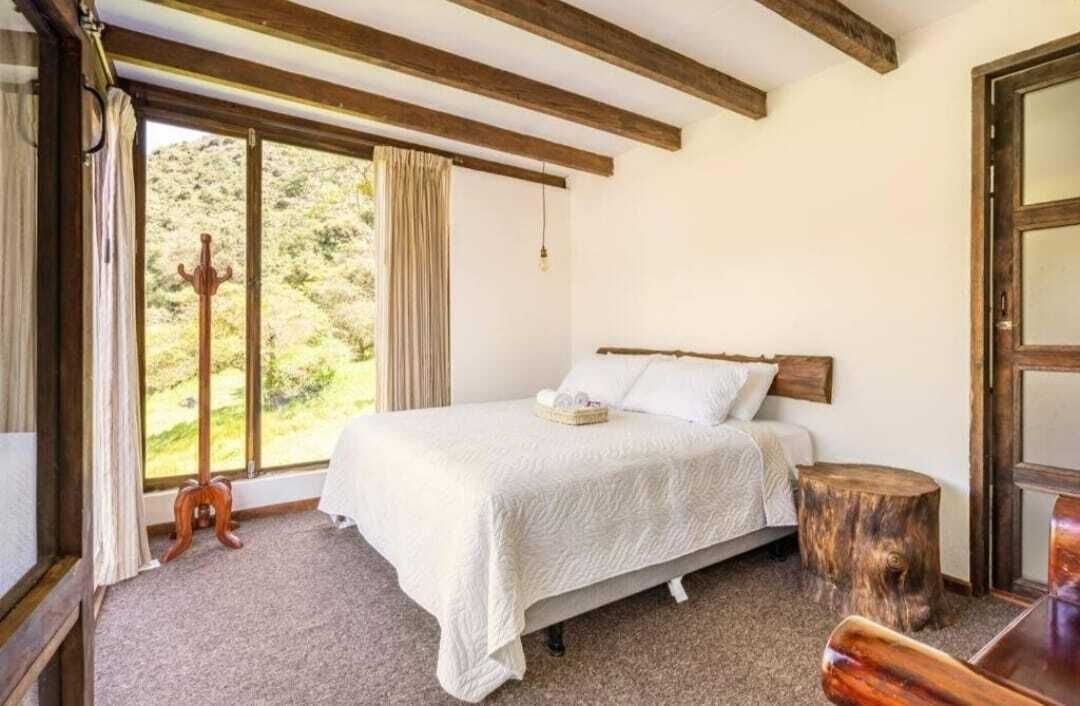 Een slaapkamer met een bed, een raam met gordijnen, een houten hoofdeinde en een klein houten krukje.